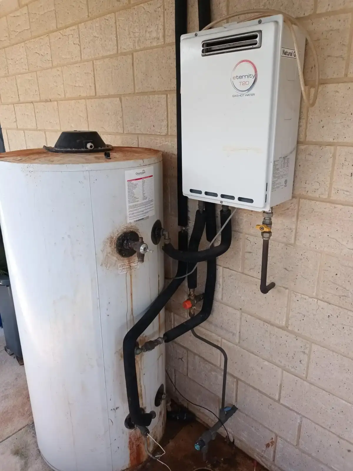 A gas continuous flow hot water unit mounted beside an old storage tank.