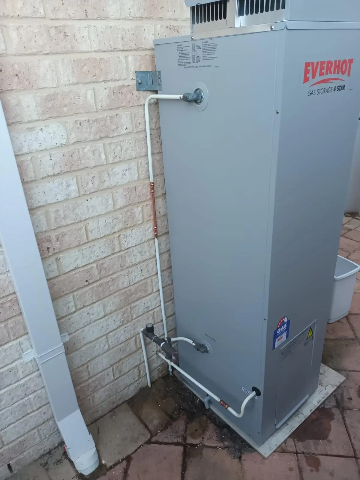 A newly connected gas storage hot water unit against a brick wall.