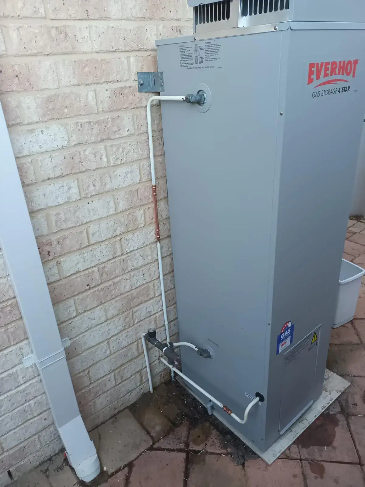 Close-up of a gas storage hot water unit against a brick wall.