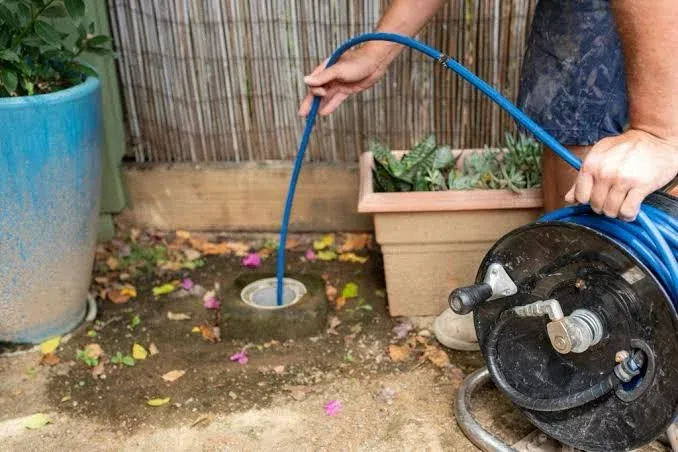 A plumber feeding a jetter hose into a blocked outdoor drain.