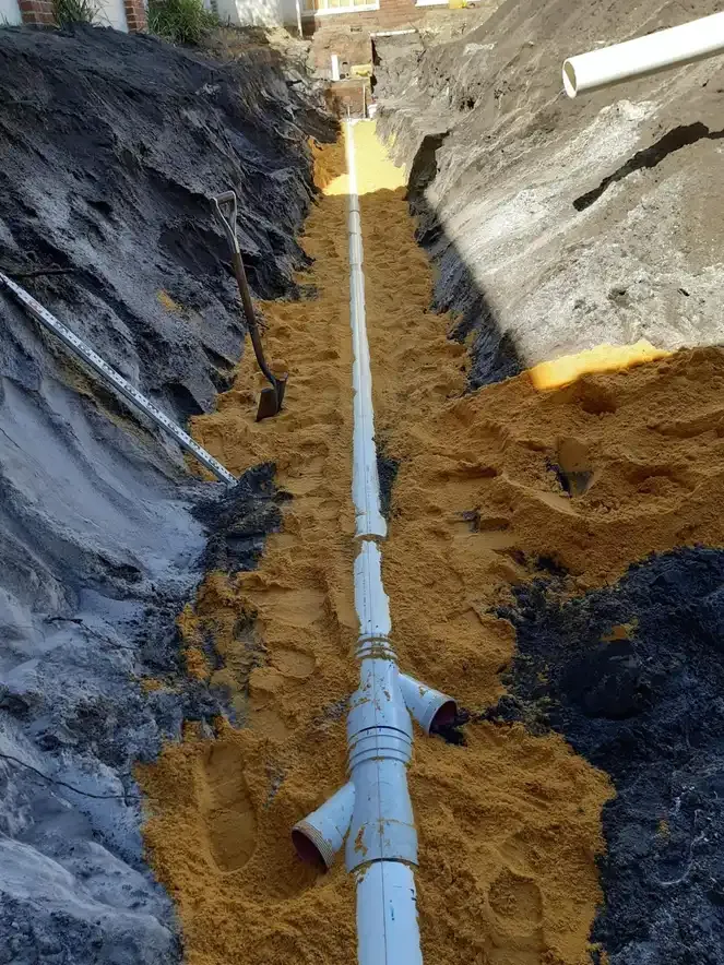 New PVC sewer pipe and junctions bedded in sand, ready for backfill.