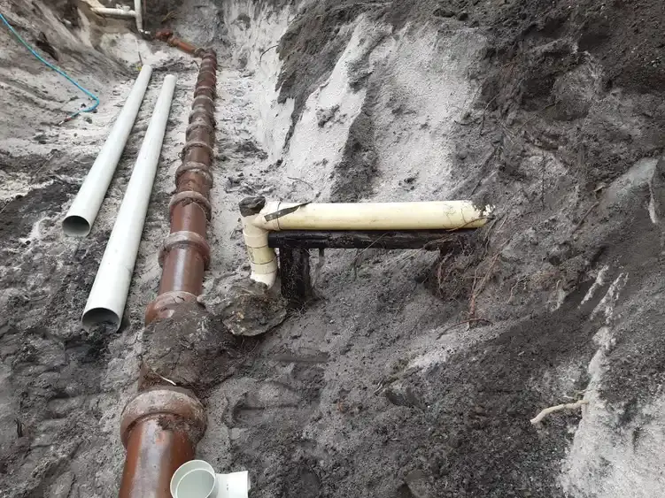 A clay sewer pipe broken open by tree roots, with new PVC pipe laid out beside it.